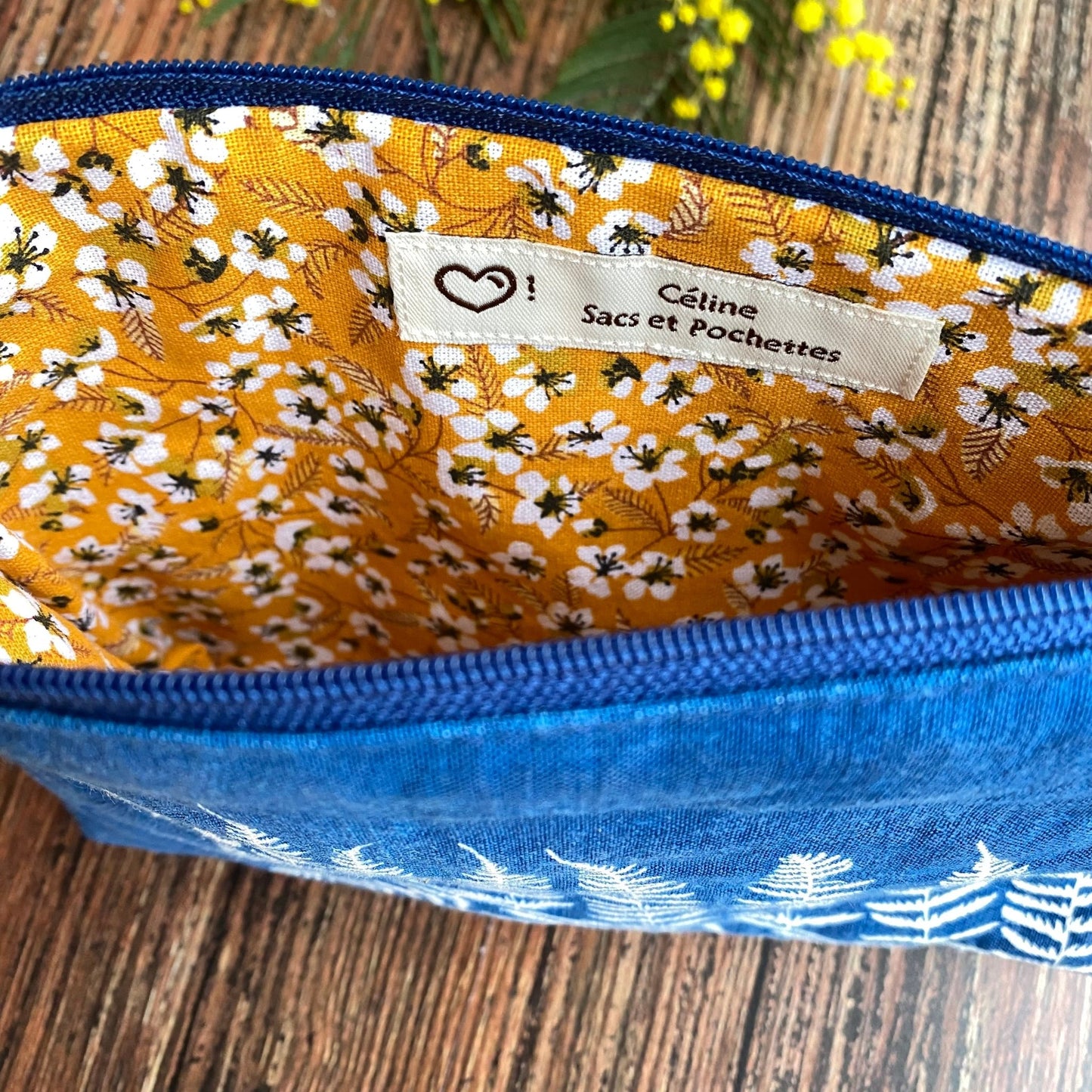 Doublure jaune d'une pochette en tissu cyanotype bleu foncée, fermeture éclair bleue, posée sur une table en bois.