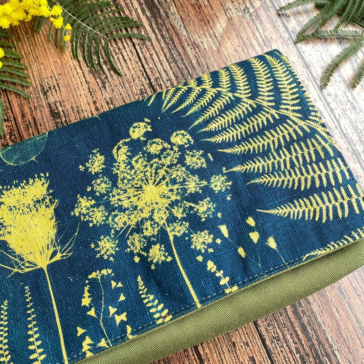 Détail d'un cyanotype sur tissu kaki utilisé pour orner le rabat d'une pochette à livre. Motifs fleurs jaunes.