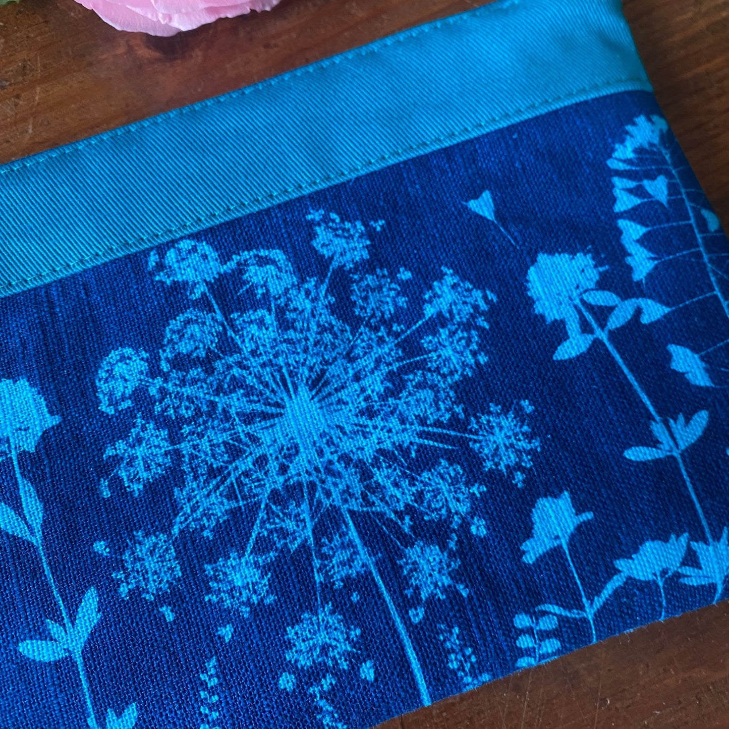 Détail d'une pochette maquillage turquoise en tissu fleuri, imprimée au cyanotype. Motifs végétaux révélés au soleil. Modèle fait main.