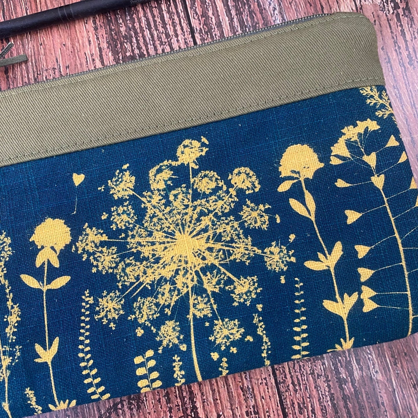 Détail d'une pochette maquillage kaki en tissu fleuri, imprimée au cyanotype. Motifs végétaux révélés au soleil. Modèle fait main.