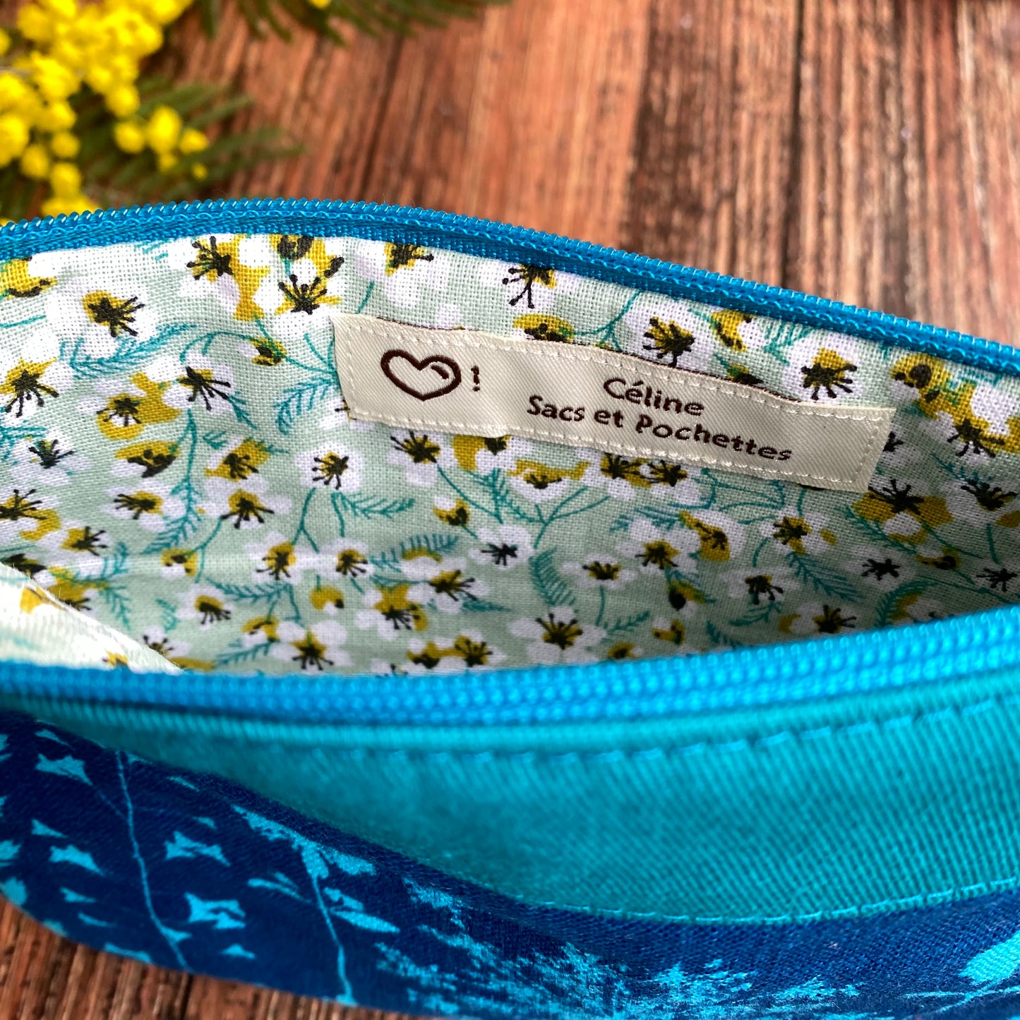 Doublure fleurie d'une pochette fait main en tissu cyanotype turquoise. Fleurs de mimosa. Etiquette artisanale.