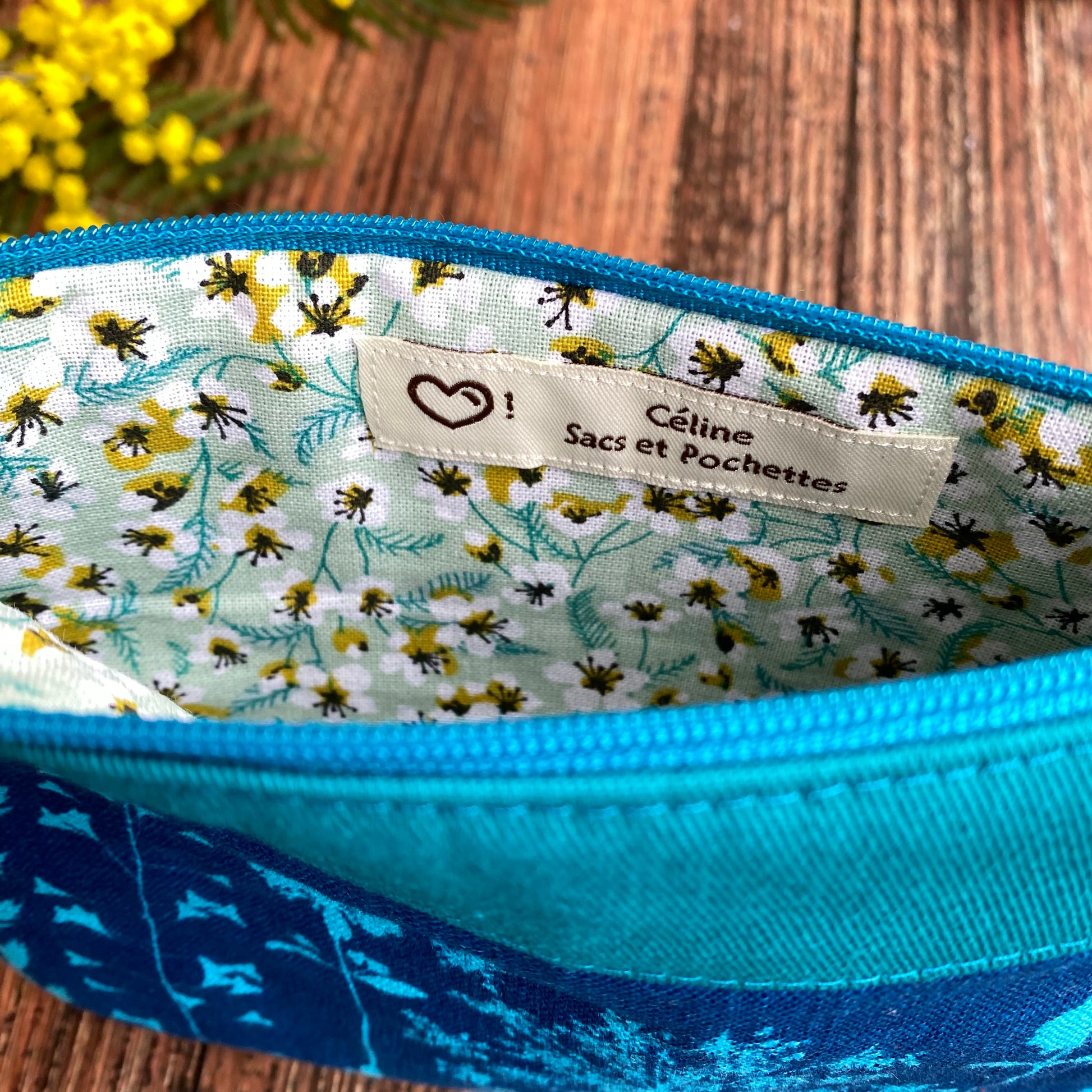 Doublure fleurie d'une pochette fait main en tissu cyanotype turquoise. Fleurs de mimosa. Etiquette artisanale.