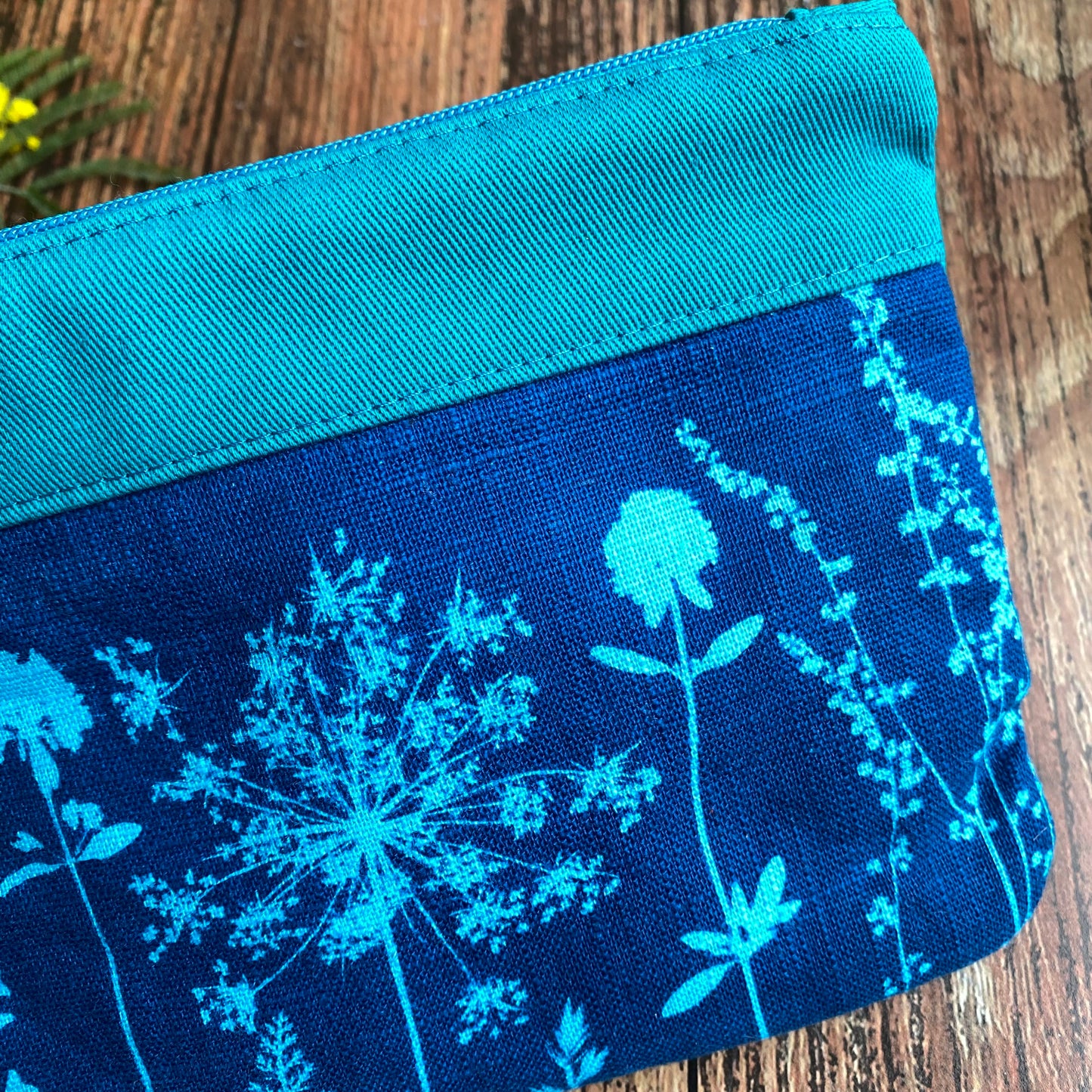 Détail d'une pochette zippée fait main, tissu imprimé de cyanotype grâce au soleil. Motifs fleurs turquoise et bleu.