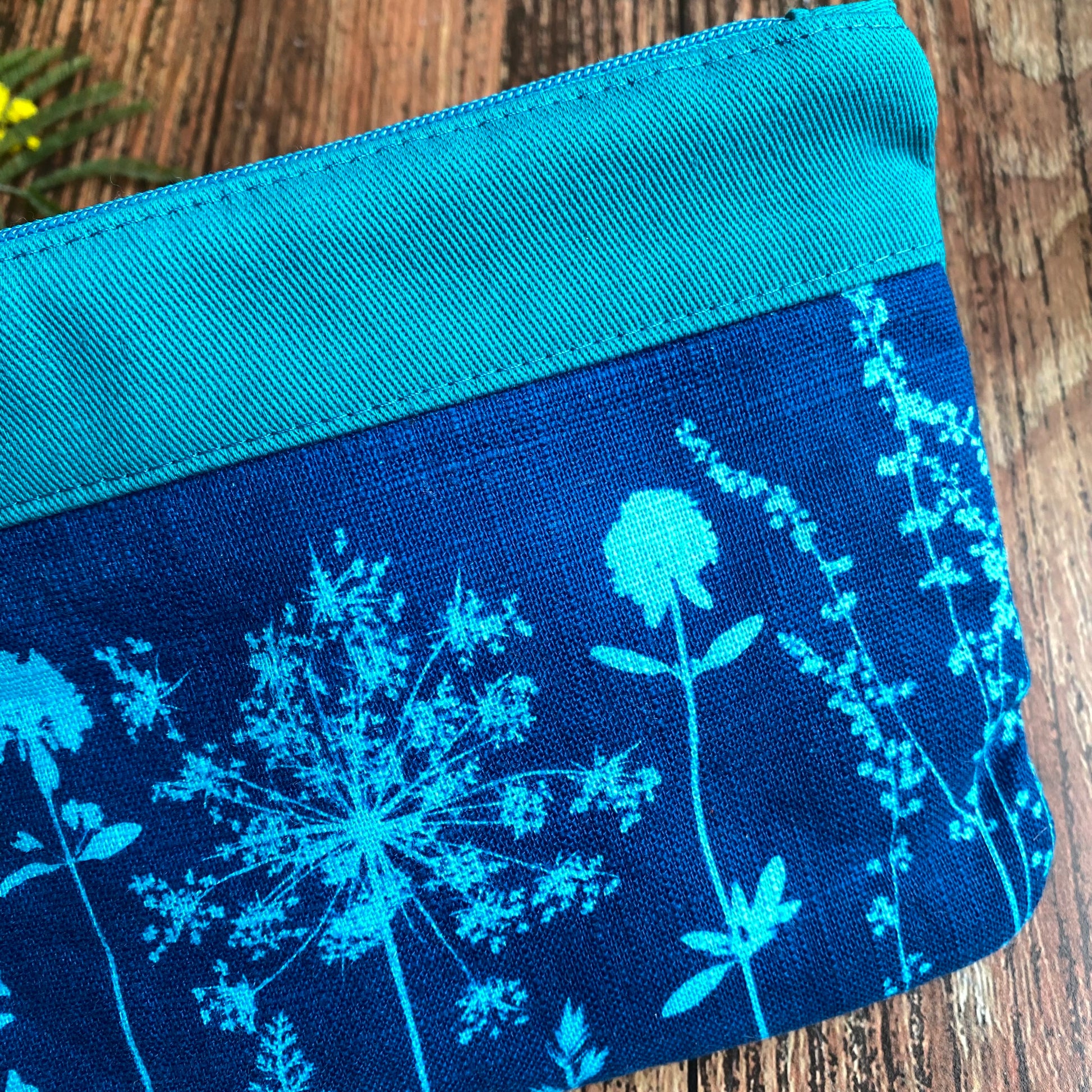 Détail d'une pochette zippée fait main, tissu imprimé de cyanotype grâce au soleil. Motifs fleurs turquoise et bleu.