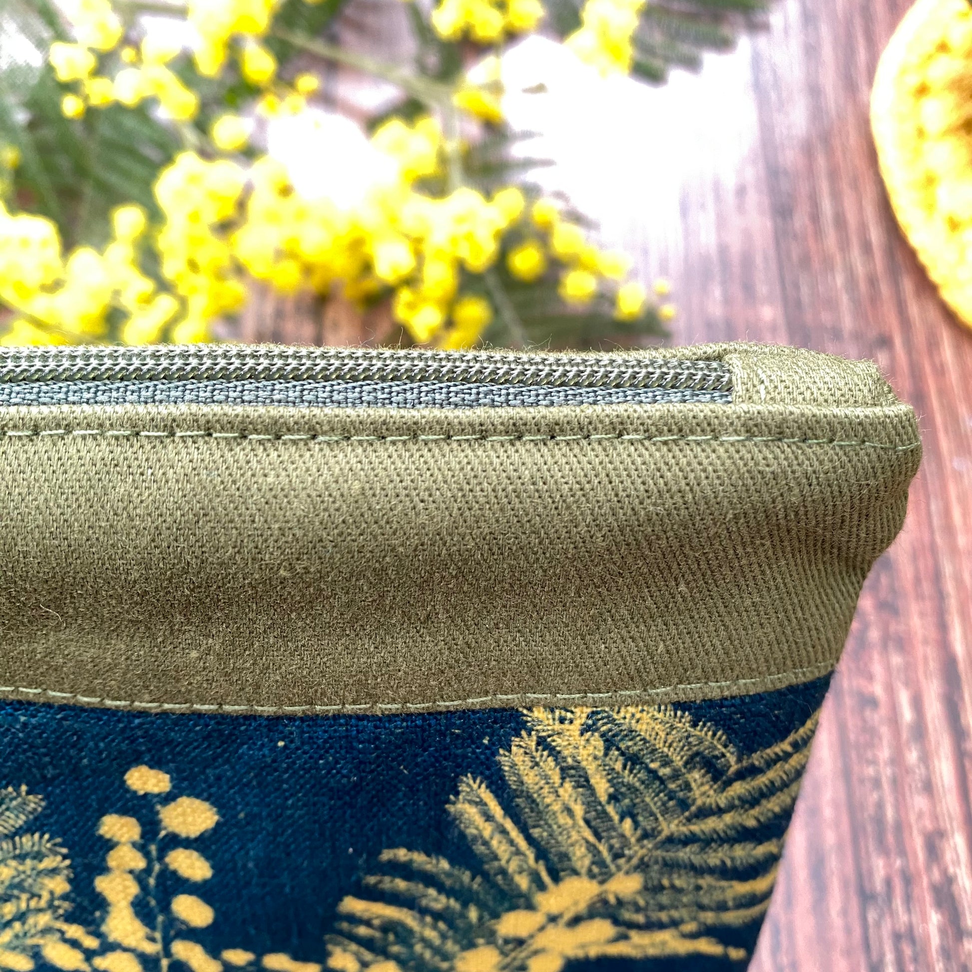 Détail d'une pochette artisanale en tissu cyanotype imprimé grace au soleil. Mimosa posé sur une table en bois.