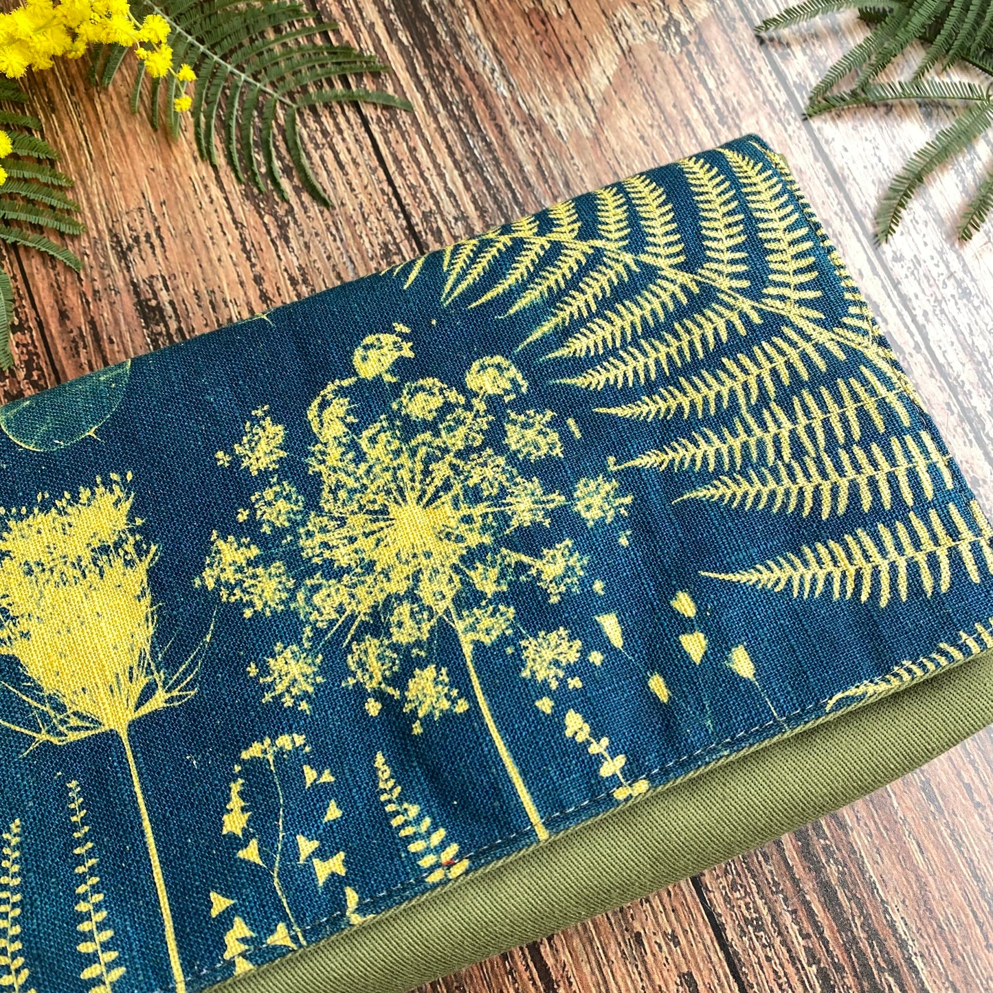 Détail d'un cyanotype sur tissu kaki utilisé pour orner le rabat d'une pochette à livre. Motifs fleurs jaunes.