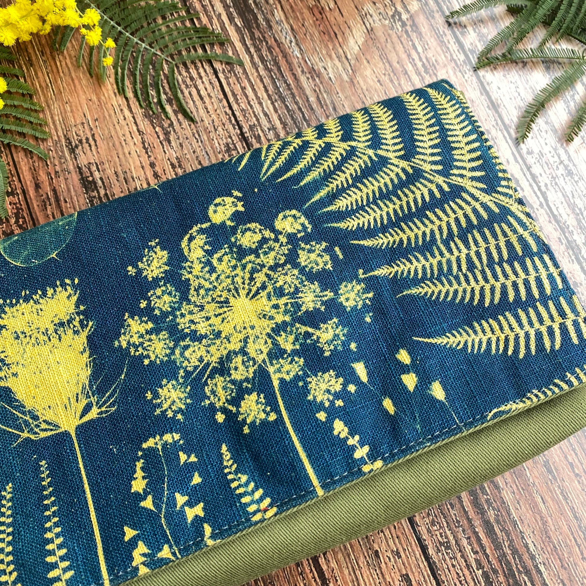 Détail d'un cyanotype sur tissu kaki utilisé pour orner le rabat d'une pochette à livre. Motifs fleurs jaunes.