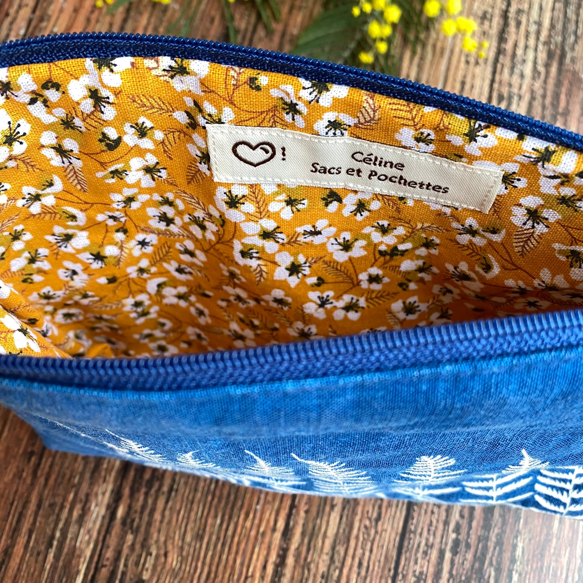 Doublure jaune d'une pochette en tissu cyanotype bleu foncée, fermeture éclair bleue, posée sur une table en bois.